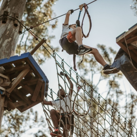 Two boys enjoying the Swinging Tarzan course with treetop obstacles like cargo nets, high ropes and crossings
