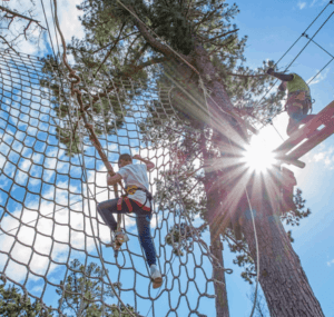 Client climbing on a cargo net during a Treetop adventure experience and instructor offering on-course support